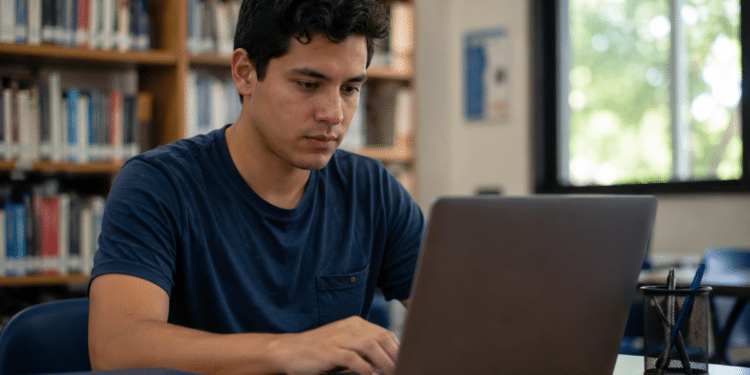 Candidato utiliza notebook em uma biblioteca para consultar oportunidades de concursos públicos com inscrições abertas.