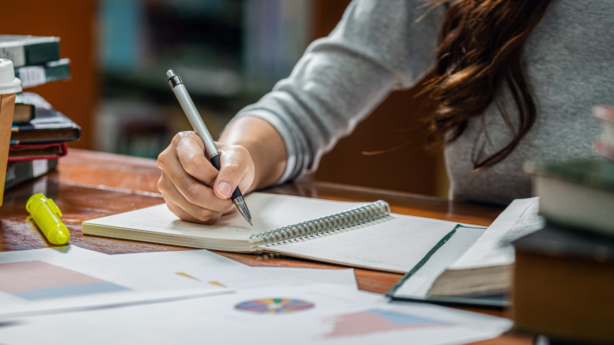 Pessoa estudando para concursos públicos com caderno e materiais de preparação sobre a mesa.