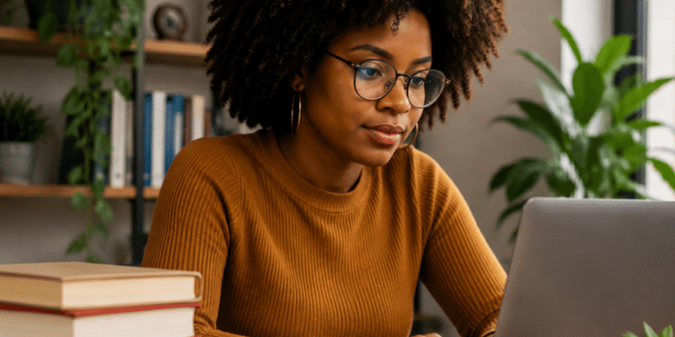 Mulher negra com cabelo afro e óculos estudando para concursos públicos usando notebook e livros em ambiente de estudo.