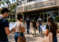 Candidatos caminham em direção a uma Câmara Municipal com documentos de concurso público.