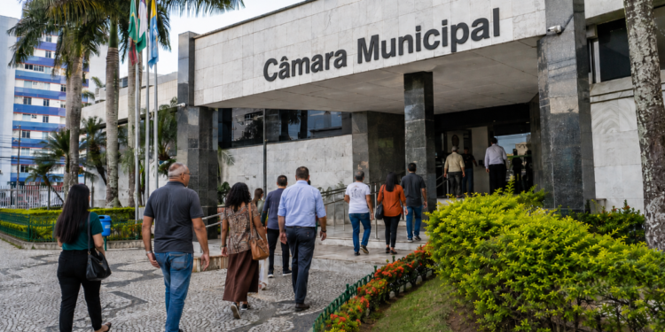 Pessoas caminham em direção a uma Câmara Municipal, em referência aos concursos públicos com vagas em SC, TO e RO.