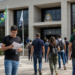 Candidatos caminham em direção a uma Câmara Municipal com mochilas, documentos e materiais de estudo para concurso público.