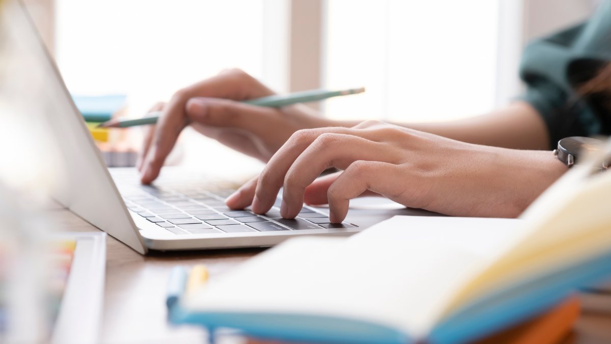 Pessoa utiliza notebook e faz anotações para acompanhar concursos públicos de nível superior.