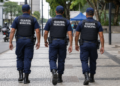 Três guardas municipais fardados caminham durante patrulhamento em área urbana.