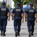 Três guardas municipais fardados caminham durante patrulhamento em área urbana.