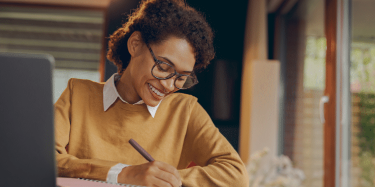 Mulher estudando em casa com caderno e notebook para concursos públicos.