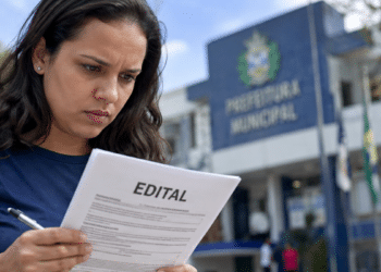 Mulher consulta edital de concurso público em frente a uma prefeitura.