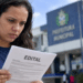 Mulher consulta edital de concurso público em frente a uma prefeitura.