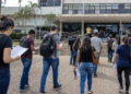 Candidatos caminham para prédio público com documentos de concursos de prefeituras.