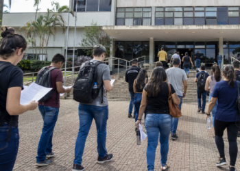 Candidatos caminham para prédio público com documentos de concursos de prefeituras.