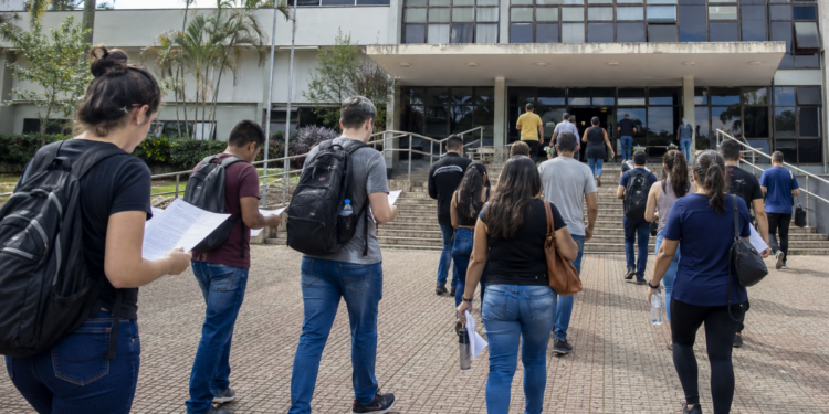 Candidatos caminham para prédio público com documentos de concursos de prefeituras.