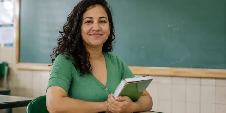Professora da rede pública segura livros em sala de aula, representando as vagas em cursos de mestrado destinadas à qualificação docente.