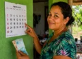 Mulher aponta para calendário de agosto enquanto segura dinheiro, representando as datas de pagamento do Bolsa Família por NIS.