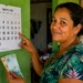 Mulher aponta para calendário de agosto enquanto segura dinheiro, representando as datas de pagamento do Bolsa Família por NIS.