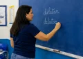Professora escreve “dilatar” e “delatar” no quadro durante aula de língua portuguesa.