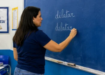 Professora escreve “dilatar” e “delatar” no quadro durante aula de língua portuguesa.