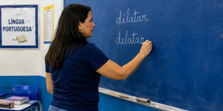 Professora escreve “dilatar” e “delatar” no quadro durante aula de língua portuguesa.