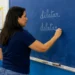 Professora escreve “dilatar” e “delatar” no quadro durante aula de língua portuguesa.
