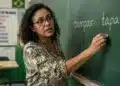 Professora de língua portuguesa em sala de aula com as palavras “tampar” e “tapar” escritas no quadro, destacando a diferença de significado entre os termos.