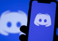 Celular exibindo o aplicativo Discord com o logotipo da plataforma ao fundo.