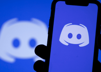 Celular exibindo o aplicativo Discord com o logotipo da plataforma ao fundo.