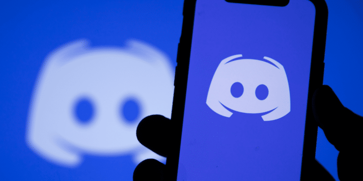 Celular exibindo o aplicativo Discord com o logotipo da plataforma ao fundo.