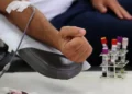 Pessoa realizando doação de sangue com coleta em bolsa e tubos para análise laboratorial.