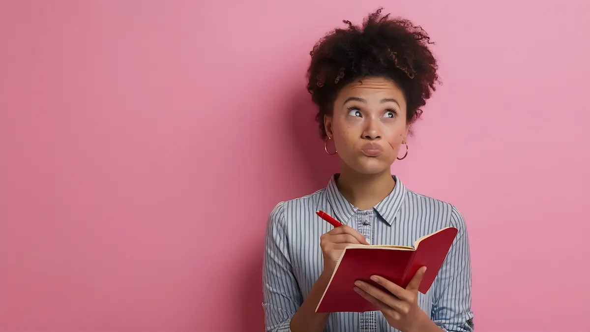 Dúvidas de Português Pessoa estudando português com caderno na mão e expressão de dúvida sobre o uso correto das palavras “trago” e “trazido”.