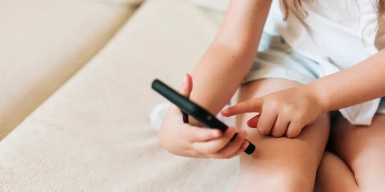 Criança utilizando smartphone em casa, representando a proteção de menores nos serviços digitais.