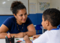 Professora acompanha criança em atividade educativa relacionada à inclusão e ao desenvolvimento.