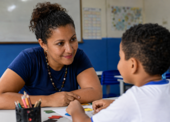 Professora acompanha criança em atividade educativa relacionada à inclusão e ao desenvolvimento.