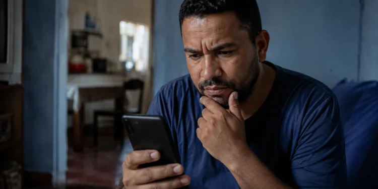 Homem observa o celular com expressão de desconfiança, representando o golpe envolvendo falso acordo do Desenrola e cobrança via Pix.