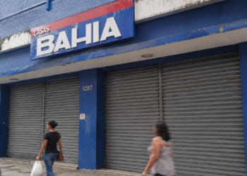 Fachada de loja da Casas Bahia com portas de ferro fechadas e pedestres passando pela calçada.