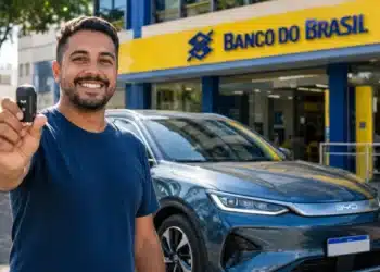 Motorista segura chave ao lado de carro elétrico BYD em frente a uma agência do Banco do Brasil.