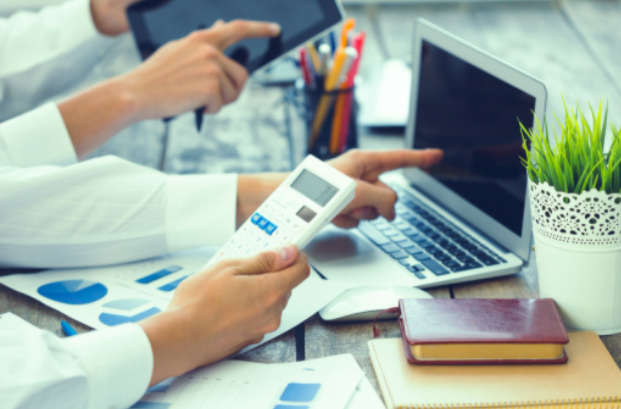 Duas pessoas analisando gráficos financeiros com calculadora, notebook e papéis em escritório