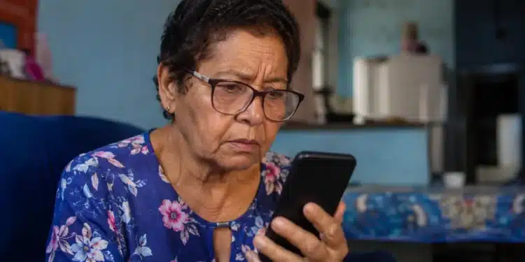 Idosa observa celular após receber mensagem suspeita sobre corte de benefício do INSS por falta de Prova de Vida.