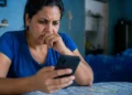 Mulher consulta o celular com expressão de preocupação, representando o possível golpe envolvendo o falso Auxílio Reconstrução de R$ 1.050.