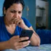 Mulher consulta o celular com expressão de preocupação, representando o possível golpe envolvendo o falso Auxílio Reconstrução de R$ 1.050.