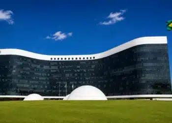 Fachada do Tribunal Superior Eleitoral em Brasília com a bandeira do Brasil ao lado, representando a criação do grupo de acompanhamento do uso de inteligência artificial e do combate às fake news nas Eleições 2026.