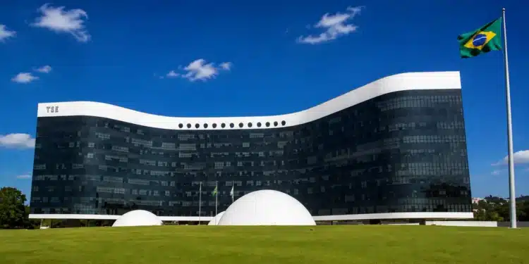 Fachada do Tribunal Superior Eleitoral em Brasília com a bandeira do Brasil ao lado, representando a criação do grupo de acompanhamento do uso de inteligência artificial e do combate às fake news nas Eleições 2026.