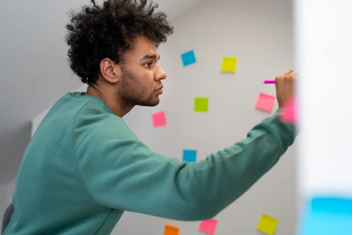 Homem concentrado escreve em painel com post-its coloridos durante uma atividade de foco intenso.