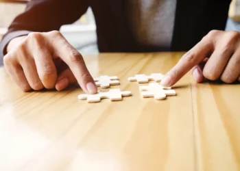 Mãos encaixam peças de quebra-cabeça sobre uma mesa, ilustrando a dúvida entre “hiperfoco” e “hiper foco”.