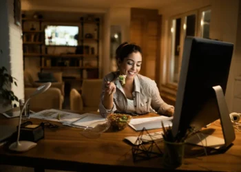 Mulher trabalhando em home office diante do computador durante uma refeição.