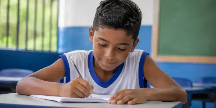 Estudante do ensino fundamental escreve em sala de aula durante atividade escolar sobre o desempenho da educação básica em tempo integral.