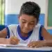 Estudante do ensino fundamental escreve em sala de aula durante atividade escolar sobre o desempenho da educação básica em tempo integral.