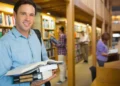 Estudante segura livros em uma biblioteca durante formação de pós-graduação.