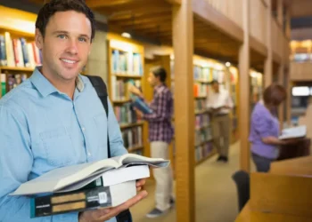 Estudante segura livros em uma biblioteca durante formação de pós-graduação.