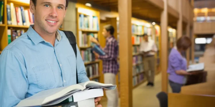 Estudante segura livros em uma biblioteca durante formação de pós-graduação.