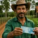 Agricultor segura cédula de R$ 100 em propriedade rural, ilustrando o acesso ao microcrédito de até R$ 15 mil para produtores.