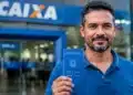 Trabalhador segura carteira de trabalho em frente a uma agência da Caixa Econômica Federal, representando a nova liberação do saque-aniversário do FGTS.